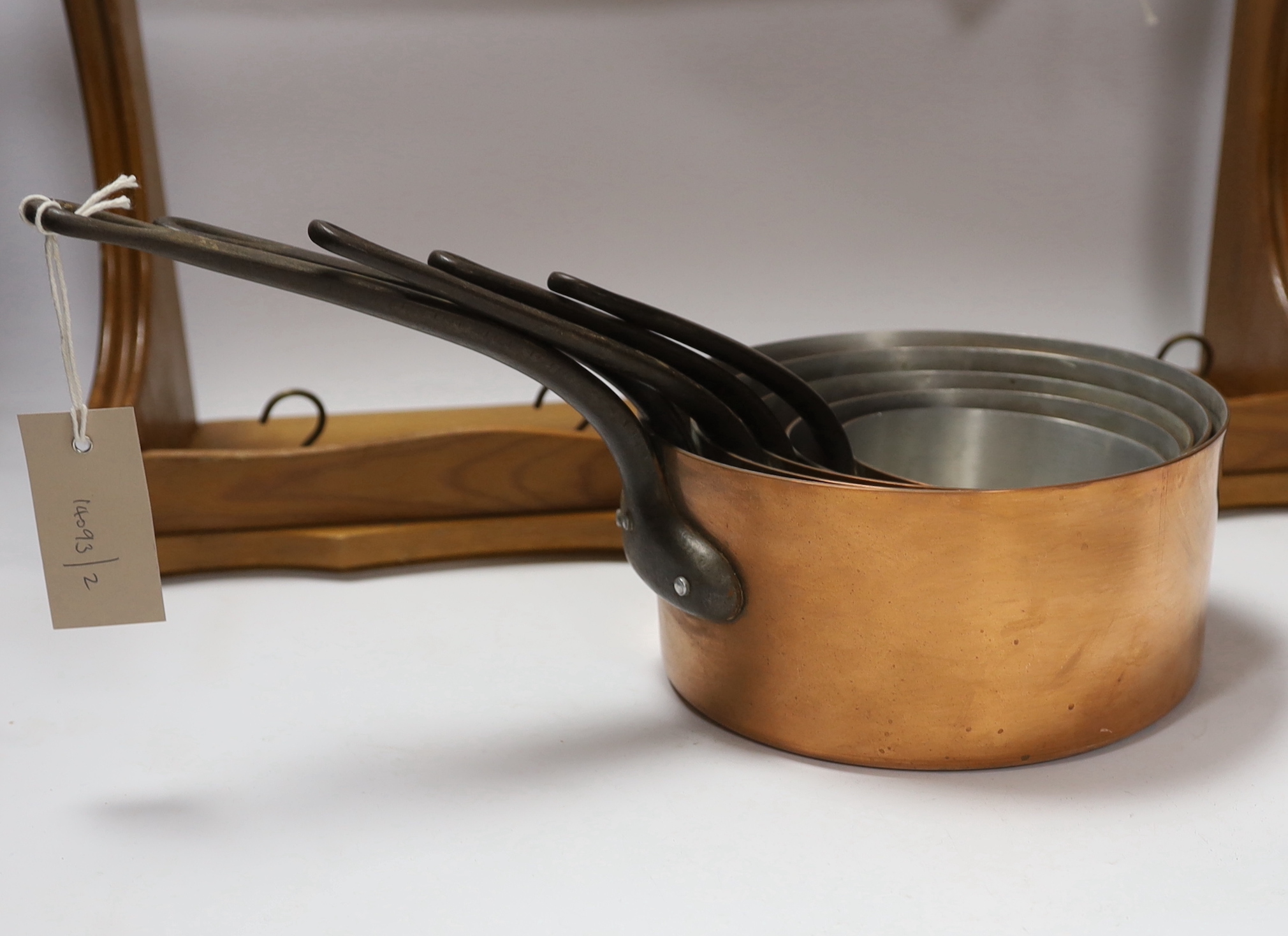 A graduated set of five French copper and cast iron saucepans with pine hanging rack, 57cm wide